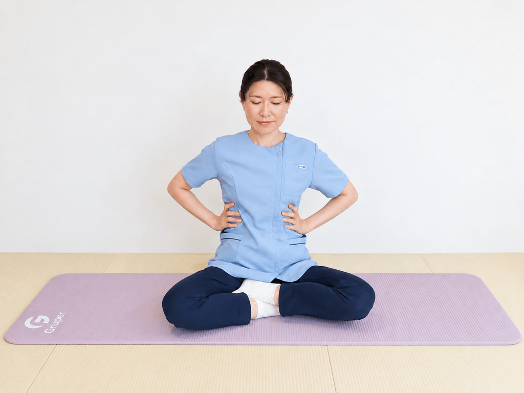 あぐらで座り、両手を肋骨の横に当てて、鼻から息を吸いながら肋骨を横と後ろに広げている様子
